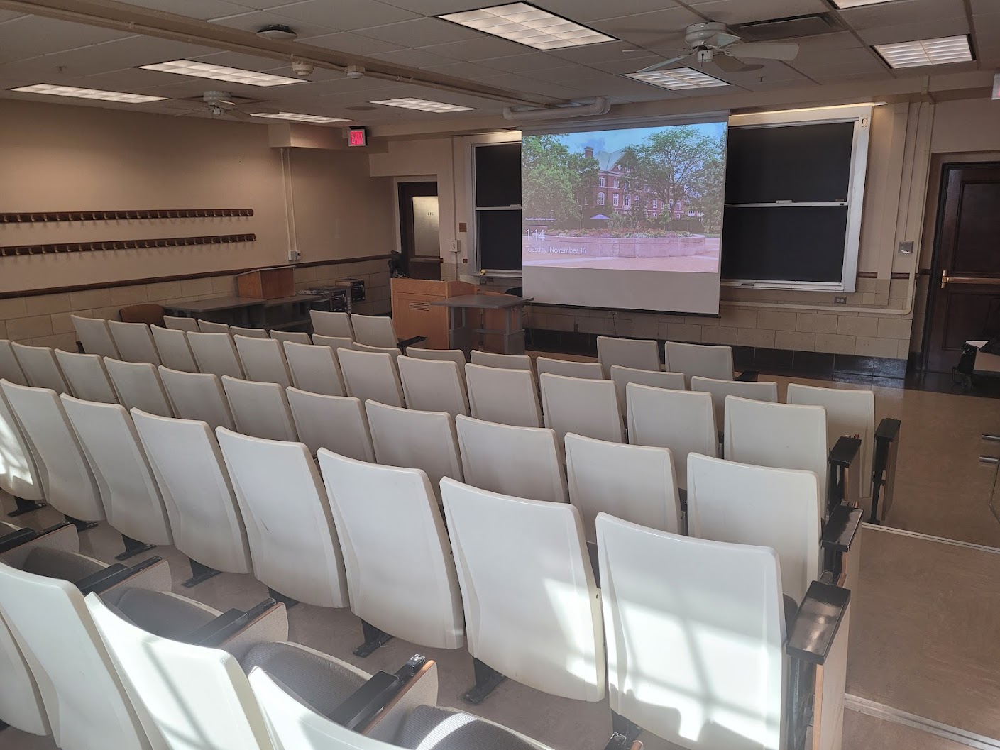 A view of the classroom with fixed auditorium seating, chalkboard, and instructor table in front.