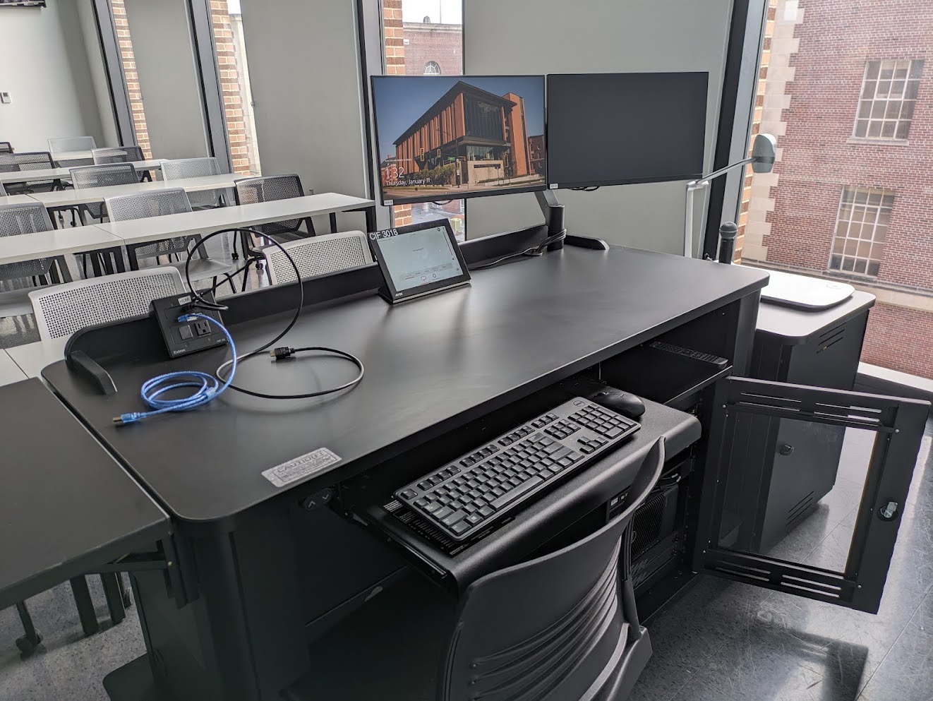 The instructor table with the control panel, keyboard, mouse, monitor, and microphone on top and the PC and sound equipment mounted underneath.