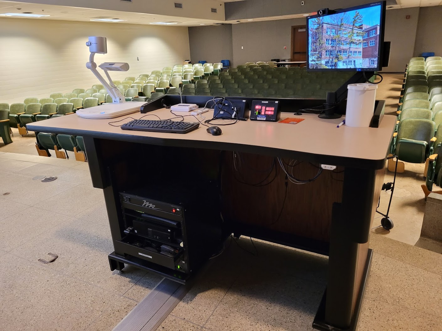 A view of the lectern with computer monitor, HDMI input, Mersive wireless, Blu-ray plater, PC, push button controller, document camera, and audio visual rack.