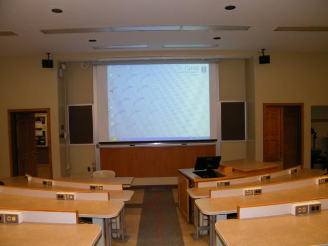A view of the classroom with tiered sloped seating, chalkboard, and large lectern in front.