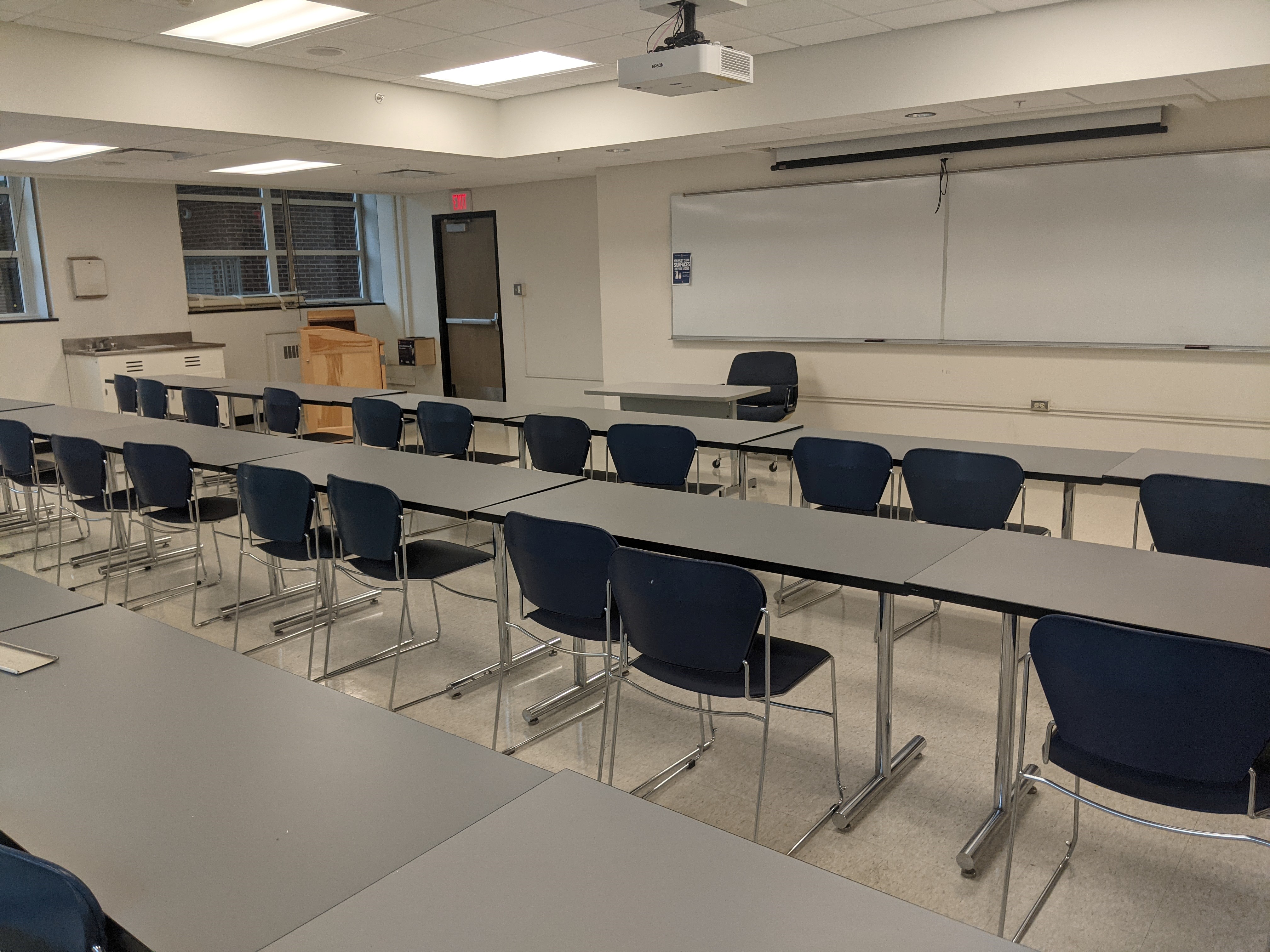 A view of the classroom with movable tables and chairs, whiteboard, and instructor table in front.