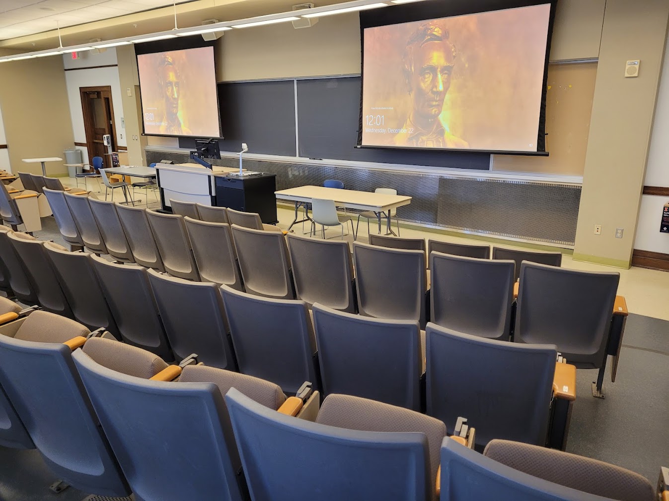 A view of the classroom with theatre auditorium seating, chalkboard, and instructor table in front.