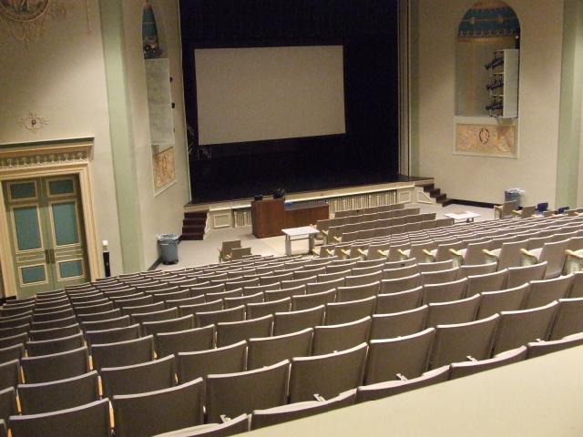 A view of the classroom with theater auditorium seating, stage, and instructor table in front.
