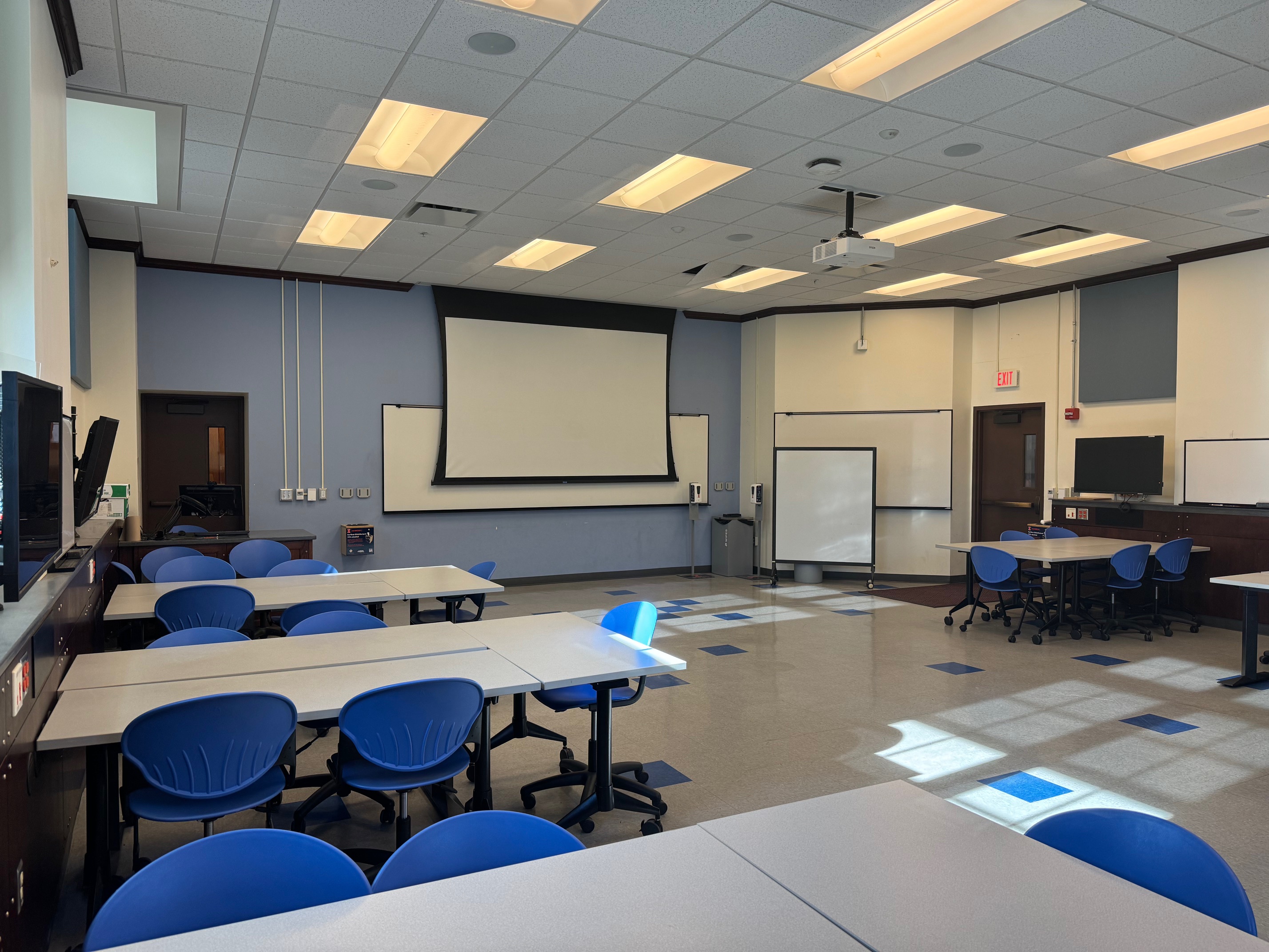 A view of the classroom with movable tables and chairs, white boards, and LCD monitors at student stations.
