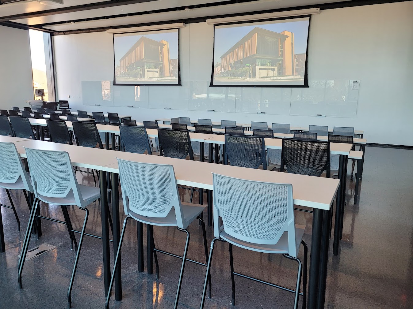 This is a view of the room with student desks, projection screens, a front lecture table, and glass boards.