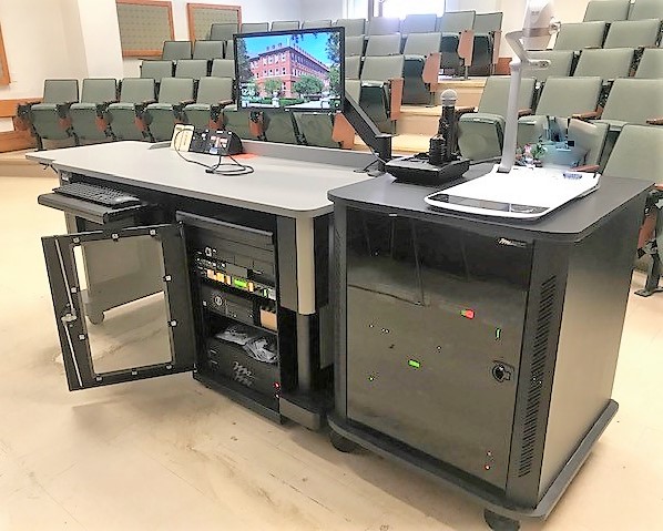 A view of the open cabinet with a computer monitor, HDMI and USB inputs, a push button controller, document camera, rechargeable microphones, audio visual rack, and electric screen controls.