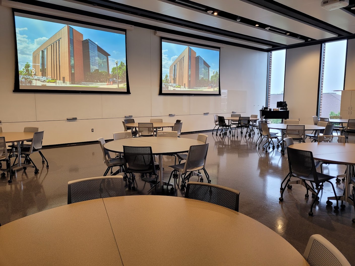 This is a view of the room with student desks, a front lecture table, and glass board