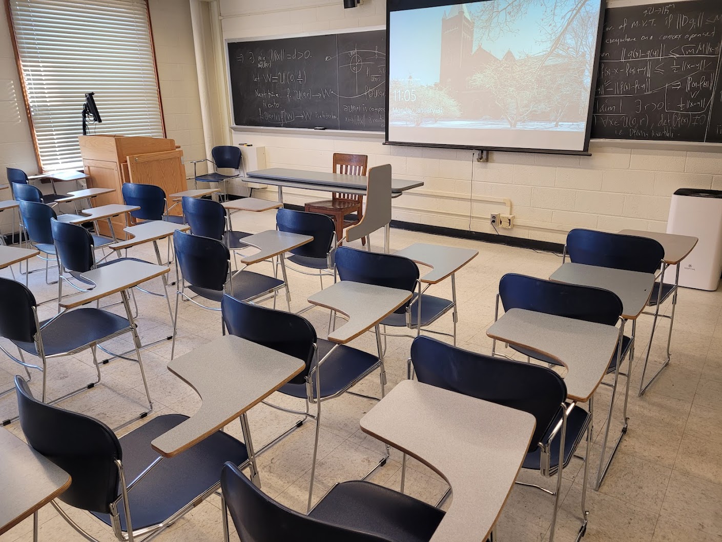 This is a view of the classroom with moveable tableted arm chairs, chalkboard, and instructor table in front.