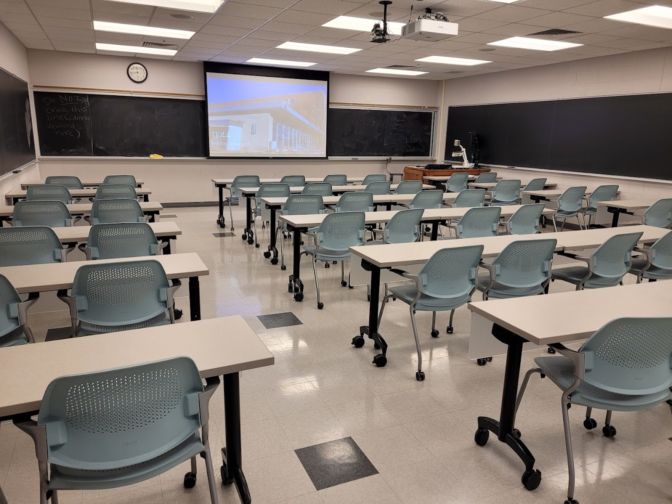 A view of the classroom with movable tables and chairs, chalkboards, and an instructor table in front.