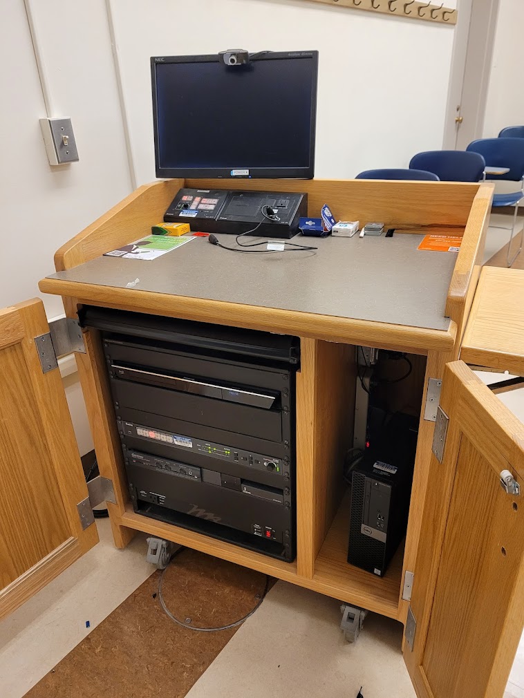 A view of the open cabinet with PC, HDMI, and Wireless inputs, a Blu-Ray DVD Player,  a push button controller, and audio visual rack.