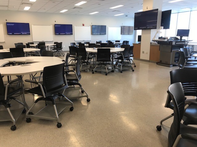 This is a view of the room, with student desks, a lectern, flat panel displays, and white boards.
