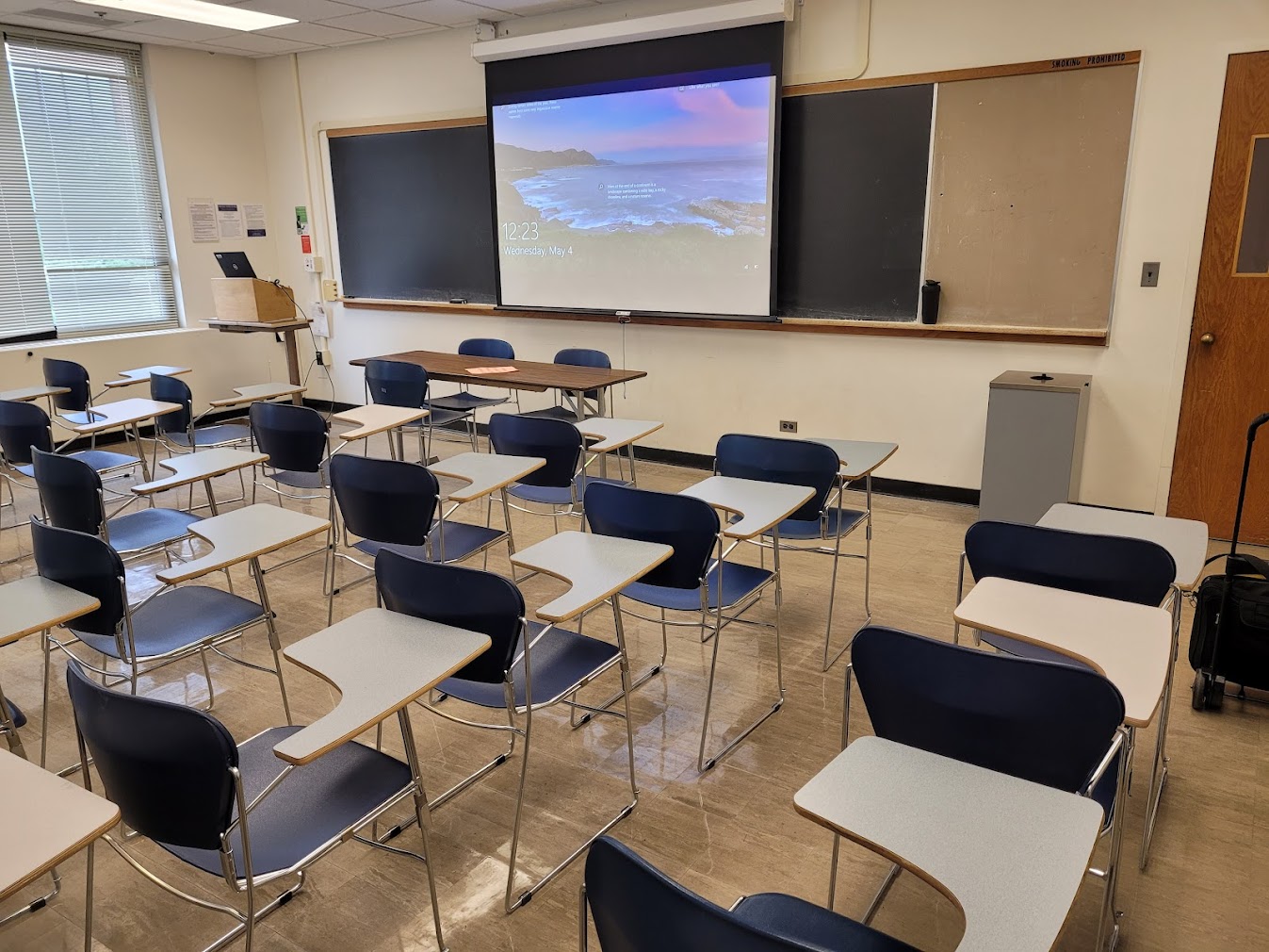 A view of the classroom with fixed tableted arm chairs and instructor table in front.