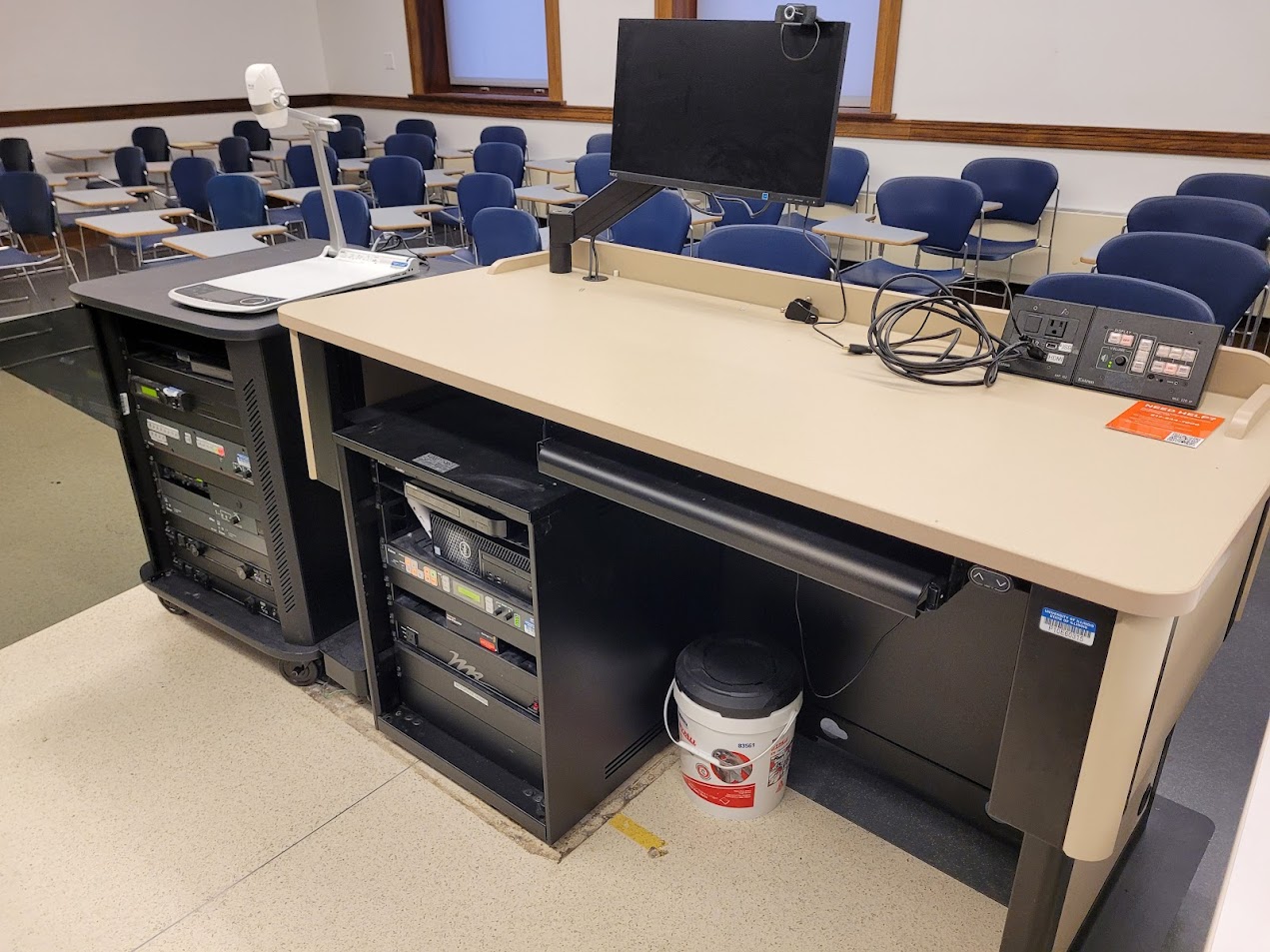 A view of the open cabinet with a computer monitor and HDMI inputs, a push button controller, document camera, and audio visual rack.