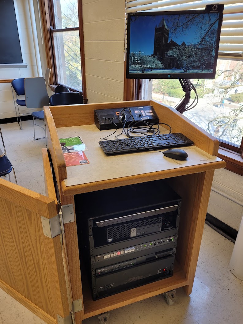 A view of the open cabinet with computer monitor, HDMI inputs, a push button controller, and audio visual rack.