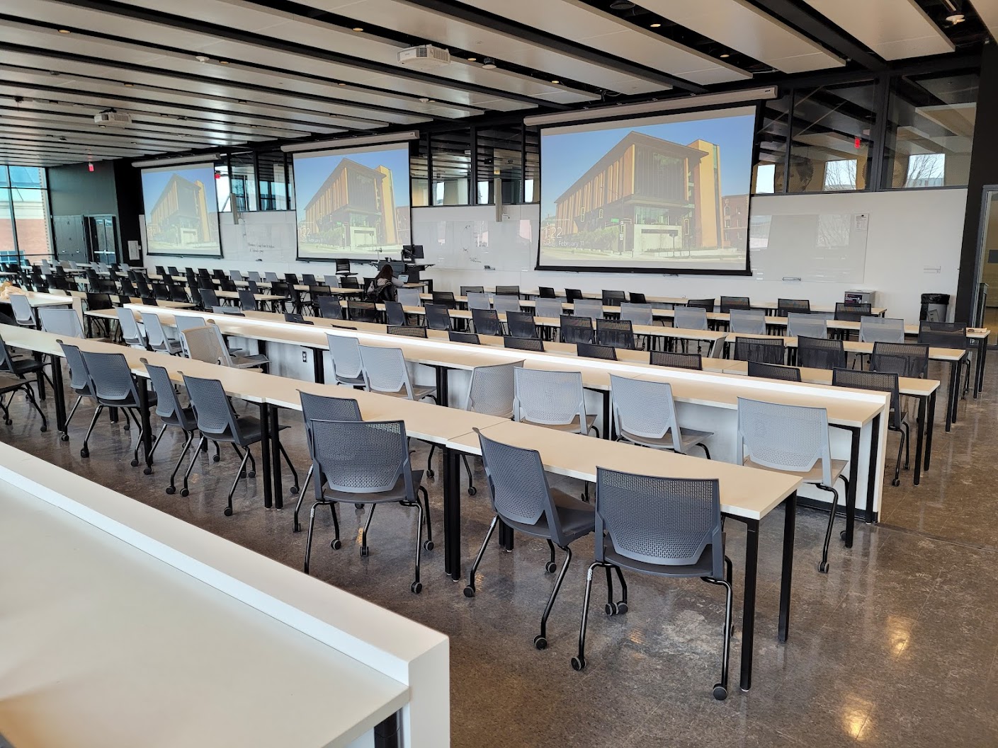 This is a view of the room, with student desks, projection screens, a front lecture table, and glass boards.