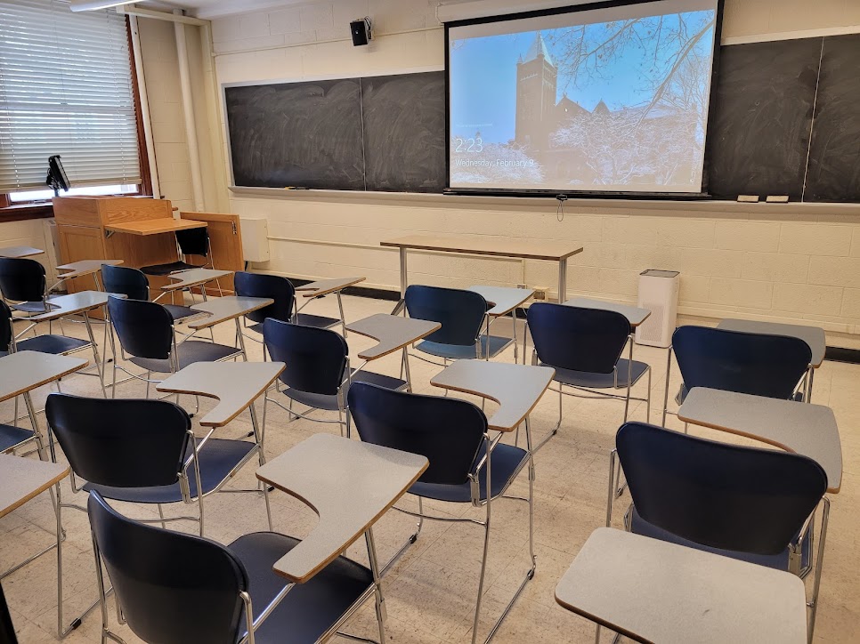 A view of the classroom with movable table arm chairs, chalkboard, and instructor table in front.