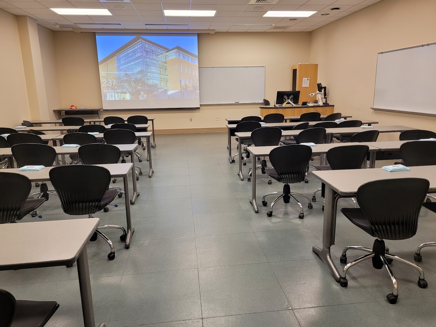 A view of the classroom with movable tables and chairs, whiteboards, and instructor table in front.