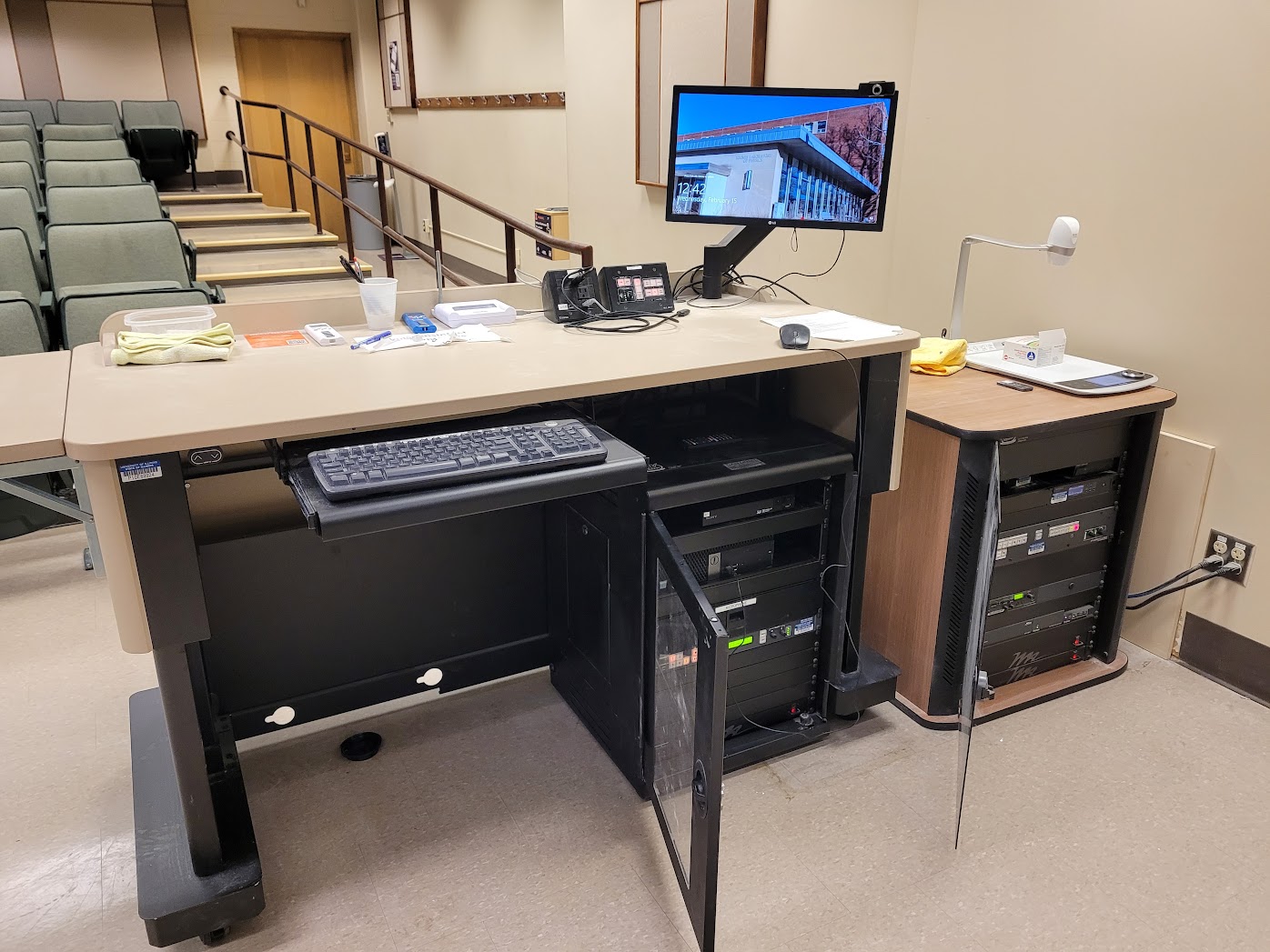 A view of the open cabinet with a computer montior, a push button controller, document camera, and audio visual rack.