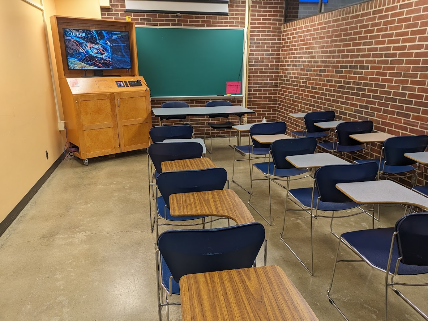 A view of the classroom with moveable tableted arm chairs, chalkboard, and an instructor table in front.