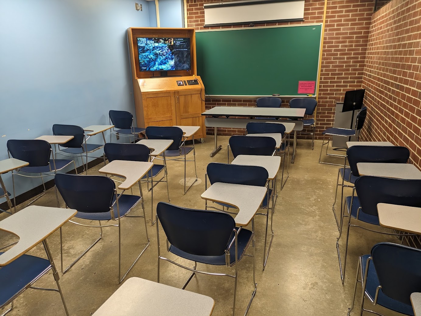 A view of the classroom with moveable tableted arm chairs, chalkboard, and instructor table in front.