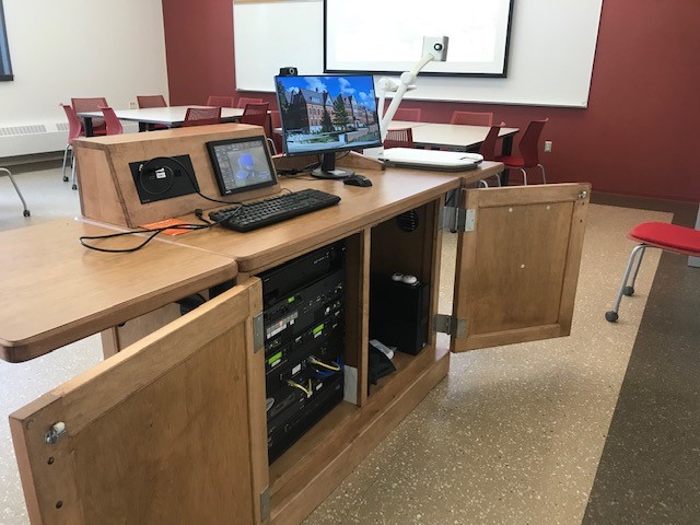 The inside of the cabinet with the control panel, document camera, keyboard, and mouse on top of the lectern and a DVD, PC, and sound equipment inside the cabinet.