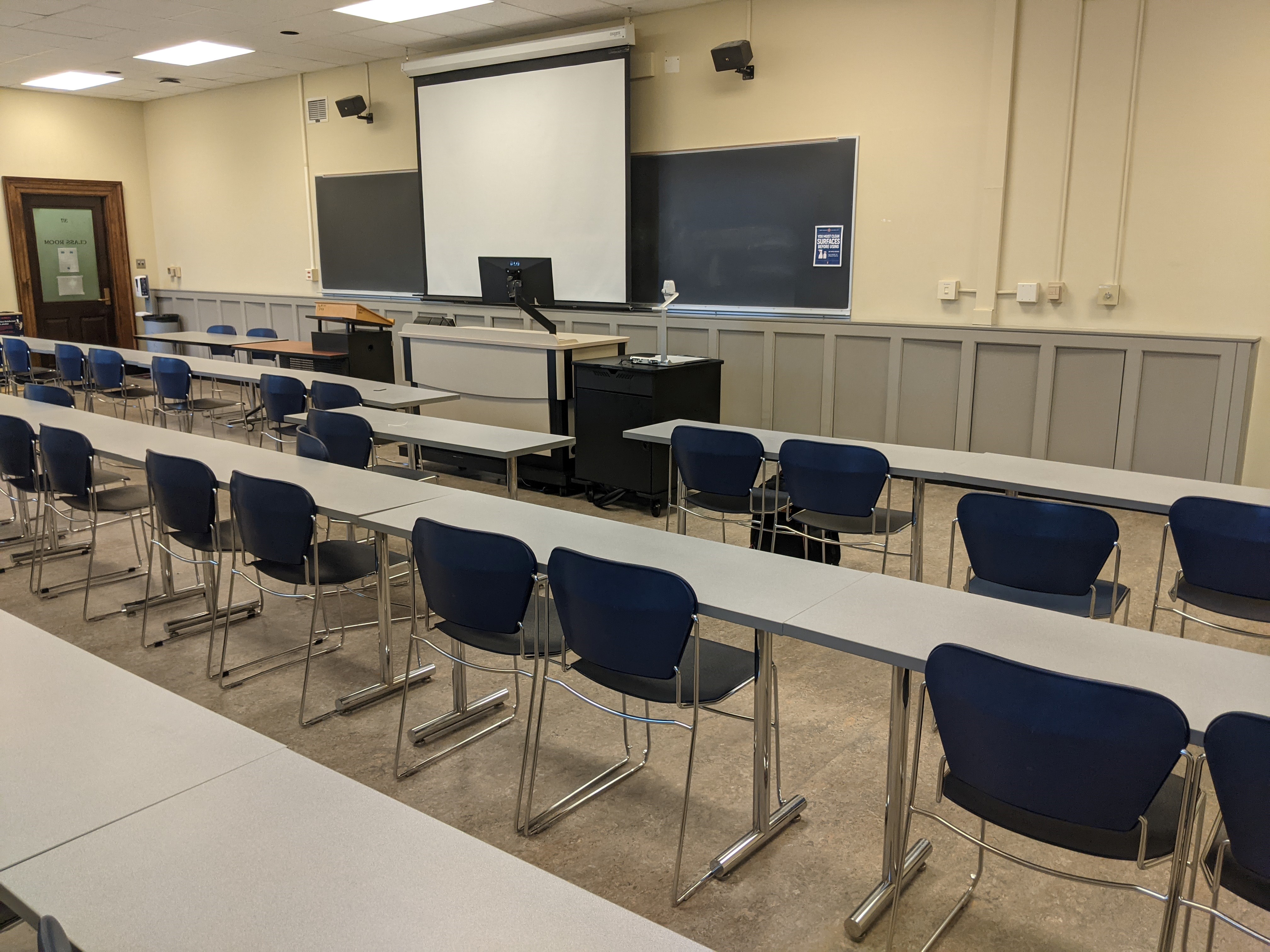 A view of the classroom with movable tables and chairs, chalkboards, and instructor table in front.