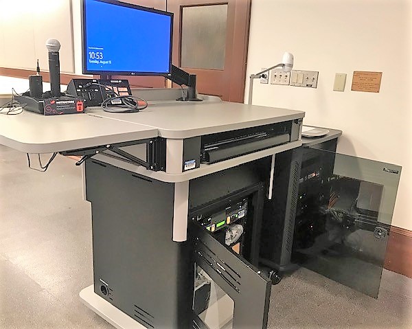 A view of the open cabinet with a computer monitor, VGA and HDMI inputs, a push button controller, document camera, audio visual rack, and electric screen controls.
