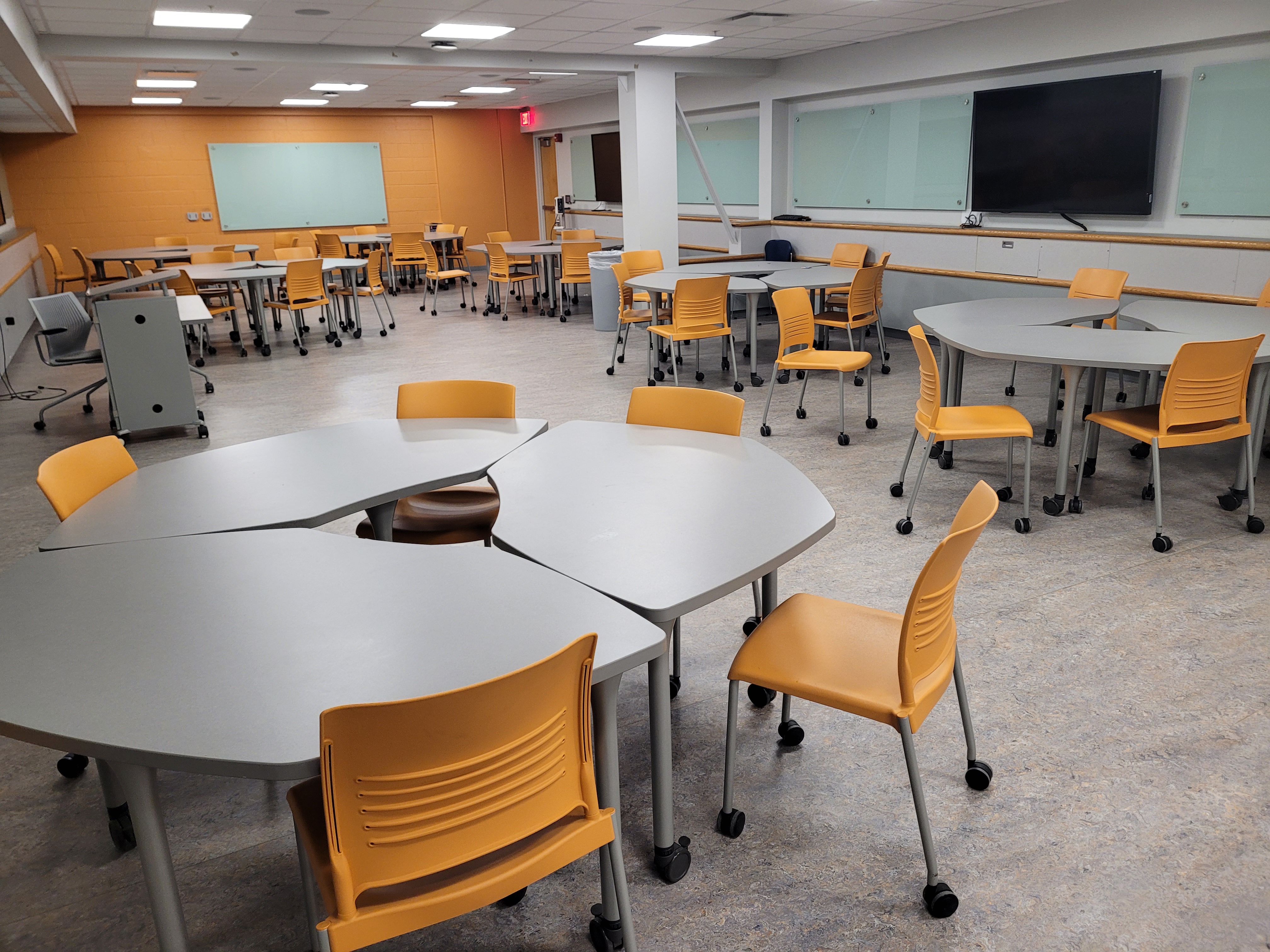 A view of the classroom with movable tables and chairs, multiple monitors, and multiple control panels mounted on the walls.