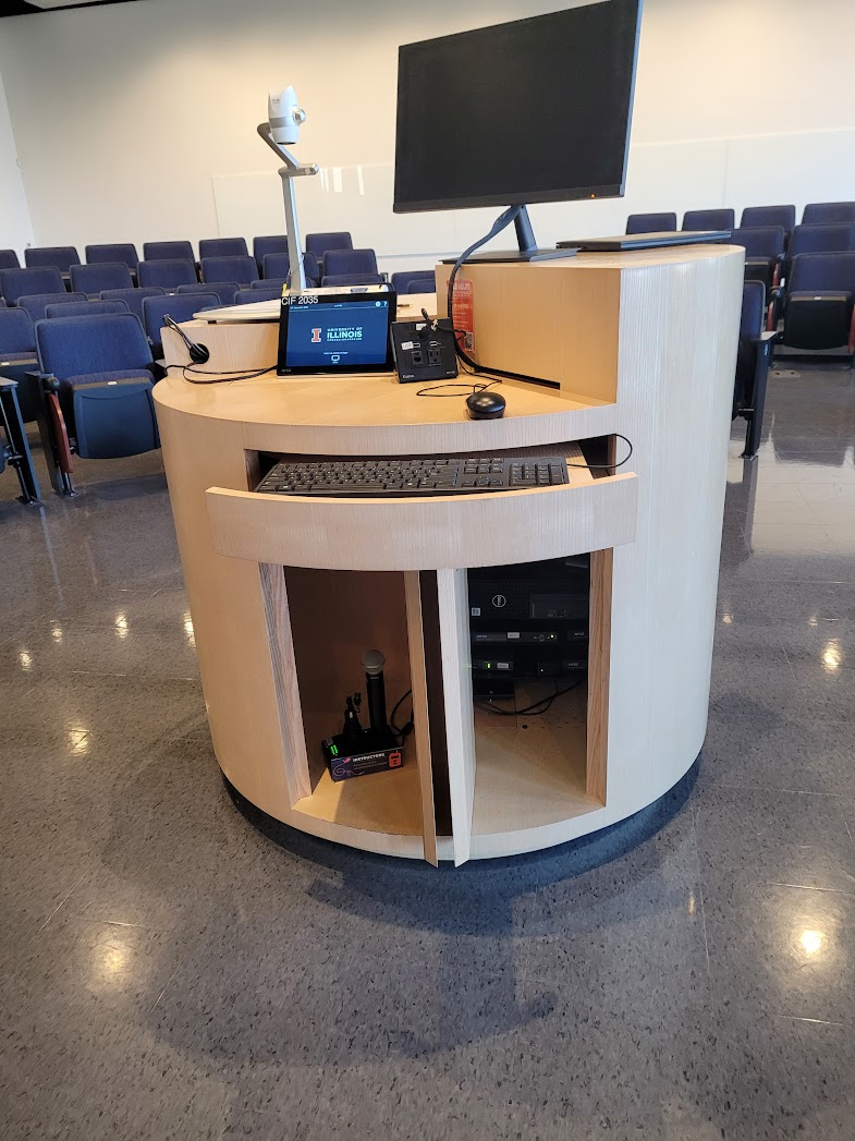 The instructor lecture table with the control panel, keyboard, mouse, monitor, document camera, and microphone on top and the PC and sound equipment mounted underneath.