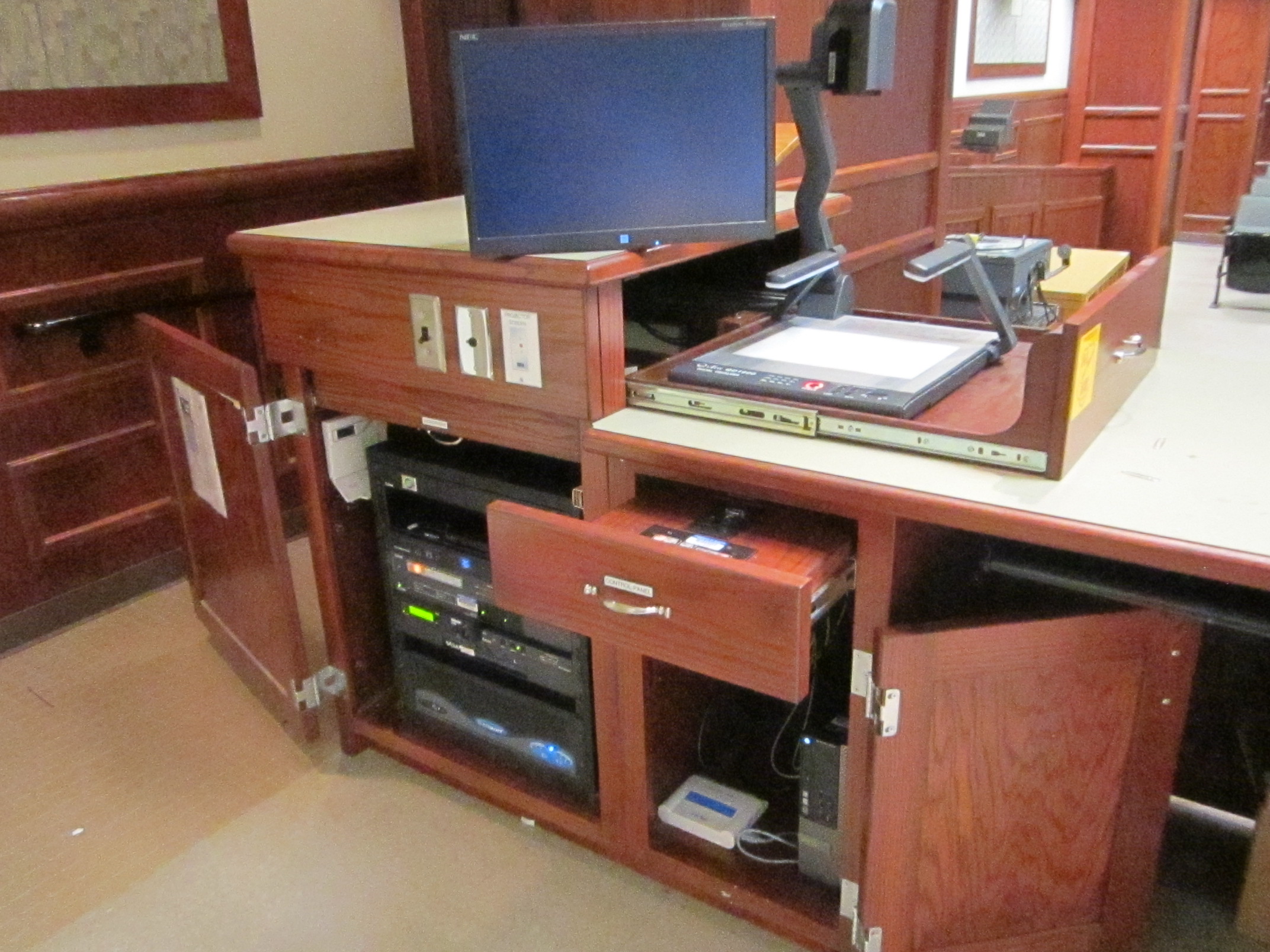 A view of the open lectern with computer monitor, HDMI input, push button controller, document camera, and audiovisual rack.