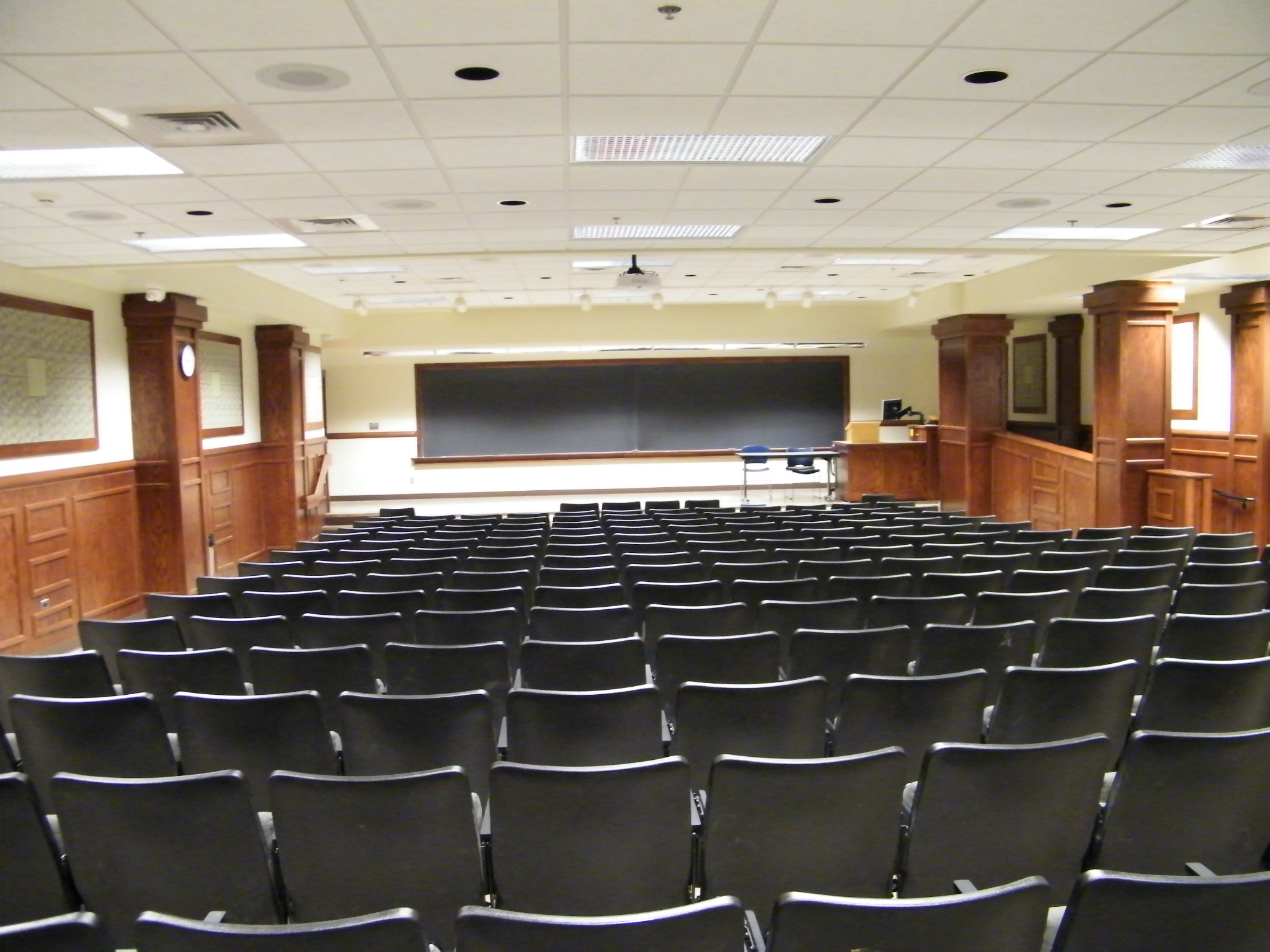 A view of the classroom with theater auditorium seating, stage, chalk board, and instructor lectern in front.