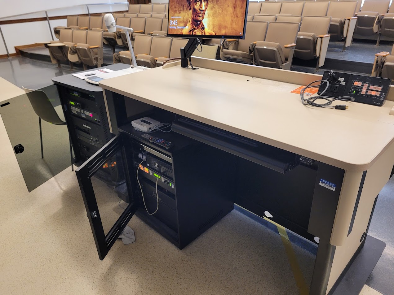 A view of the open cabinet with a computer monitor, HDMI inputs, a push button controller, document camera, and audio visual rack.
