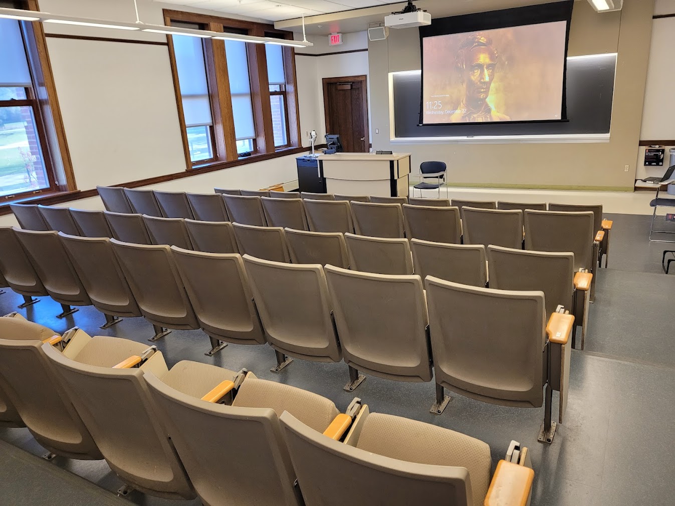 A view of the classroom with theatre auditorium seating, chalkboard, and instructor table in front.