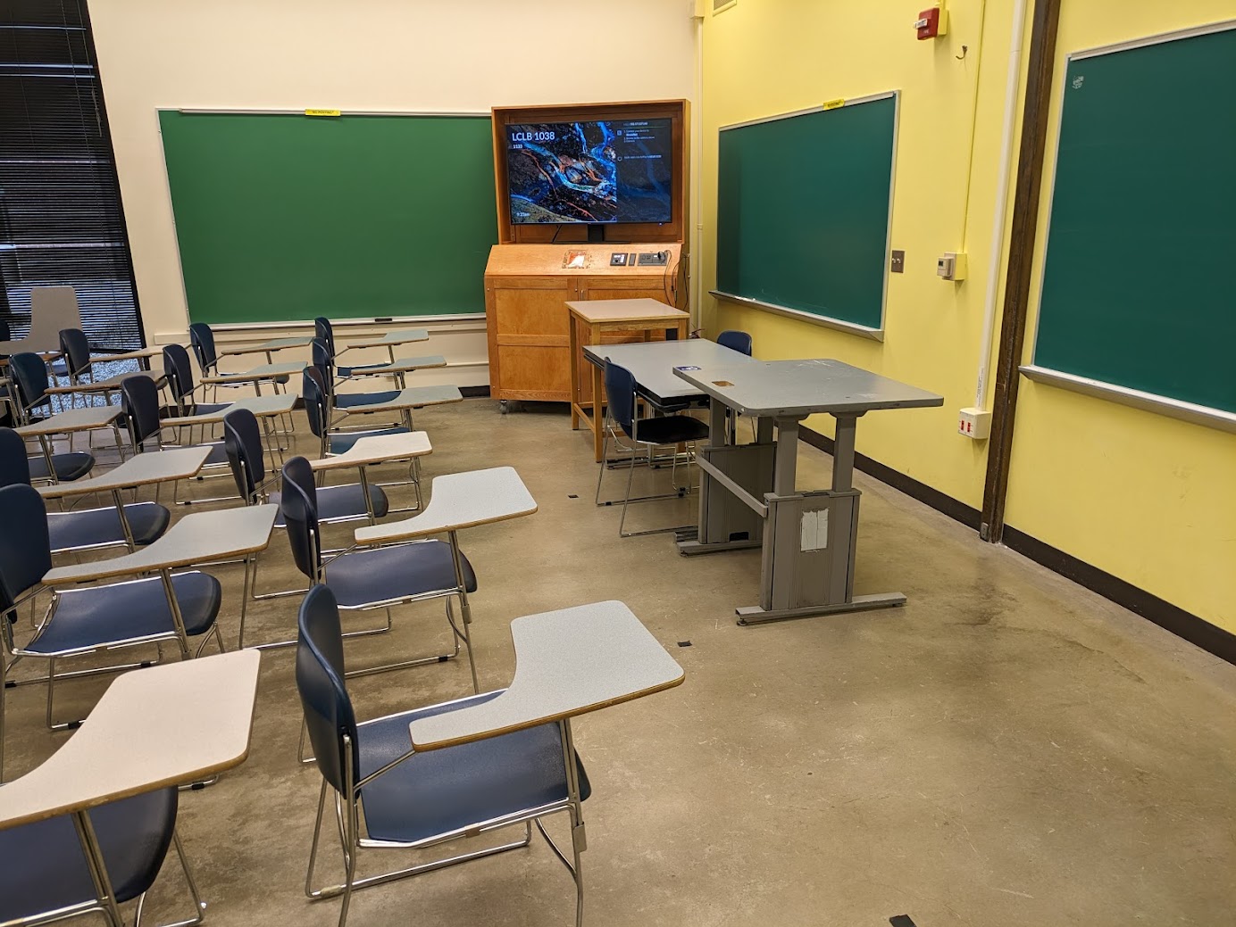 A view of the classroom with movable tableted arm chairs, chalkboards and instructor table in font.