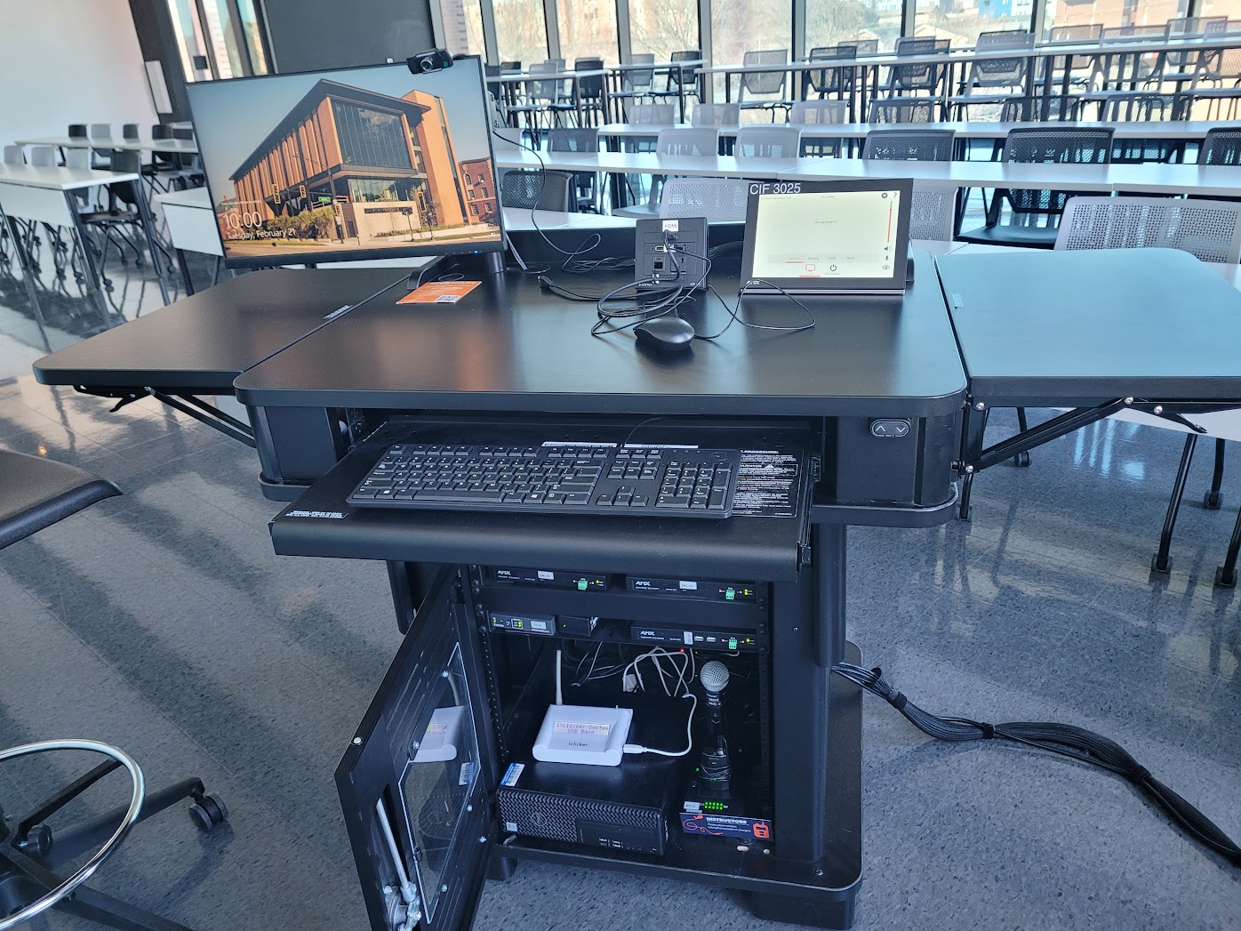 The instructor lectern with the control panel, keyboard, mouse, and monitor on top and the PC, microphones, and sound equipment.