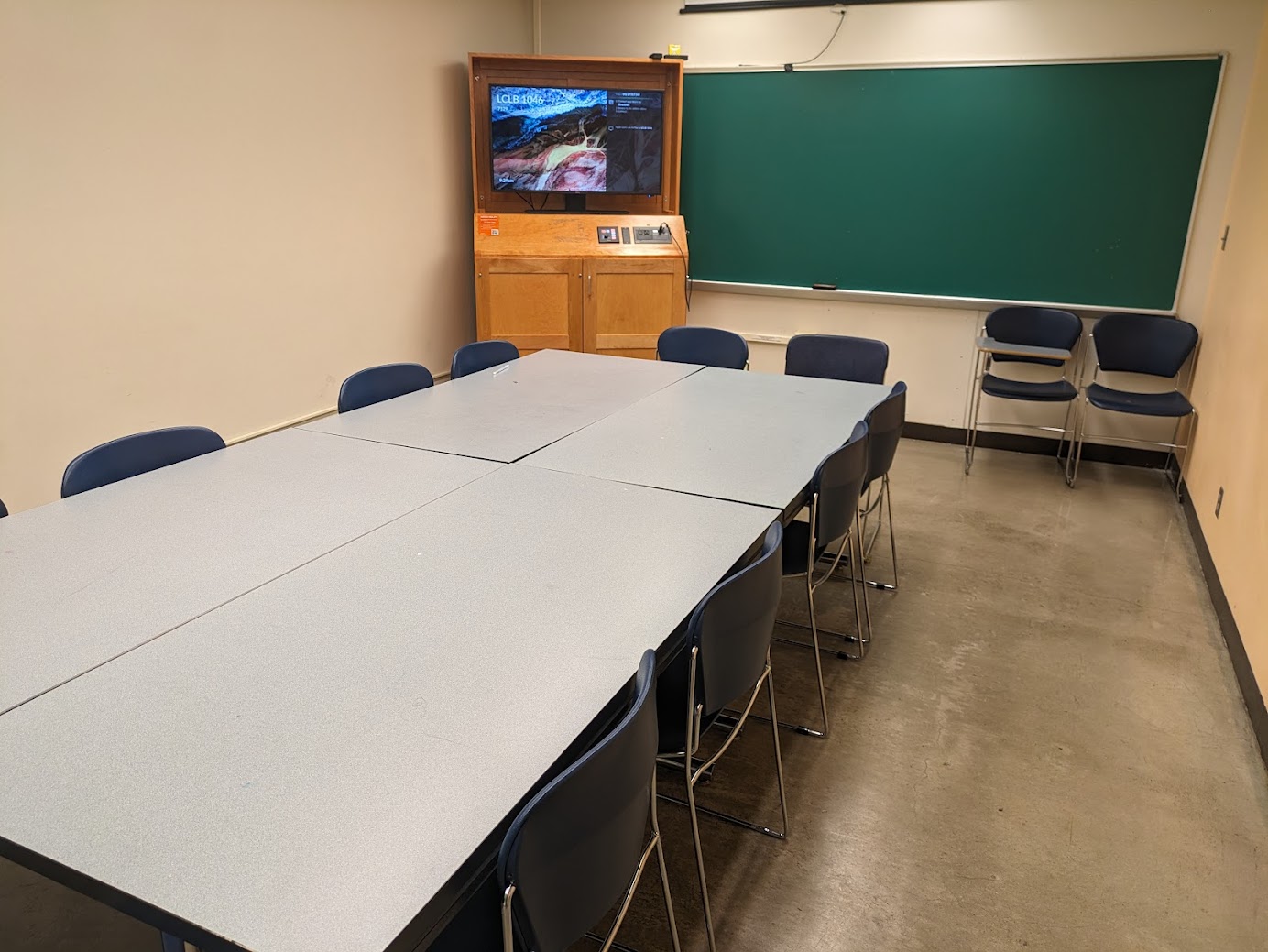 A view of the classroom with conference style student seating, a high definition LCD monitor, and a chalkboard