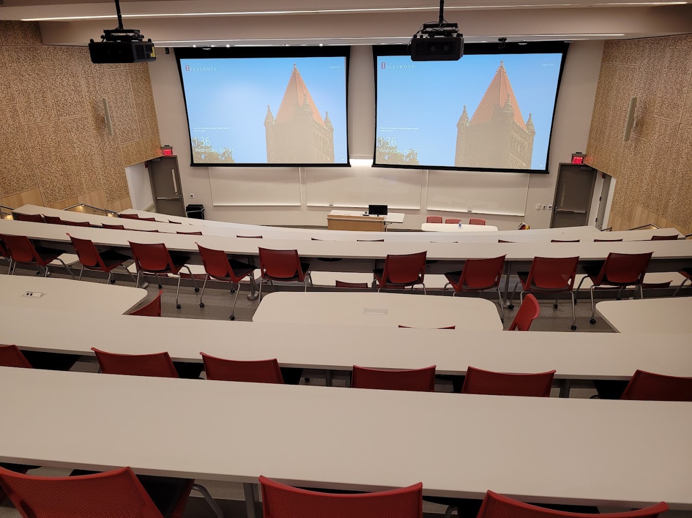 This is a view of the room, with student desks and tables, a front lectern, projection screen, and white boards.