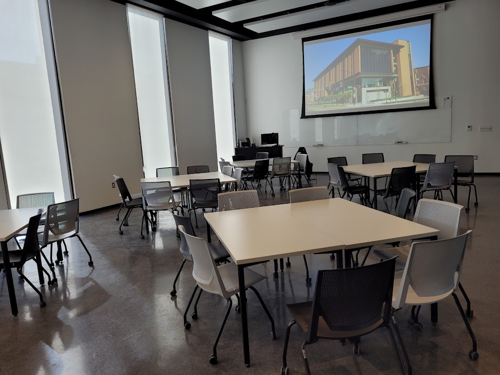 This is a view of the room with student desks, a front lecture table, and white boards.