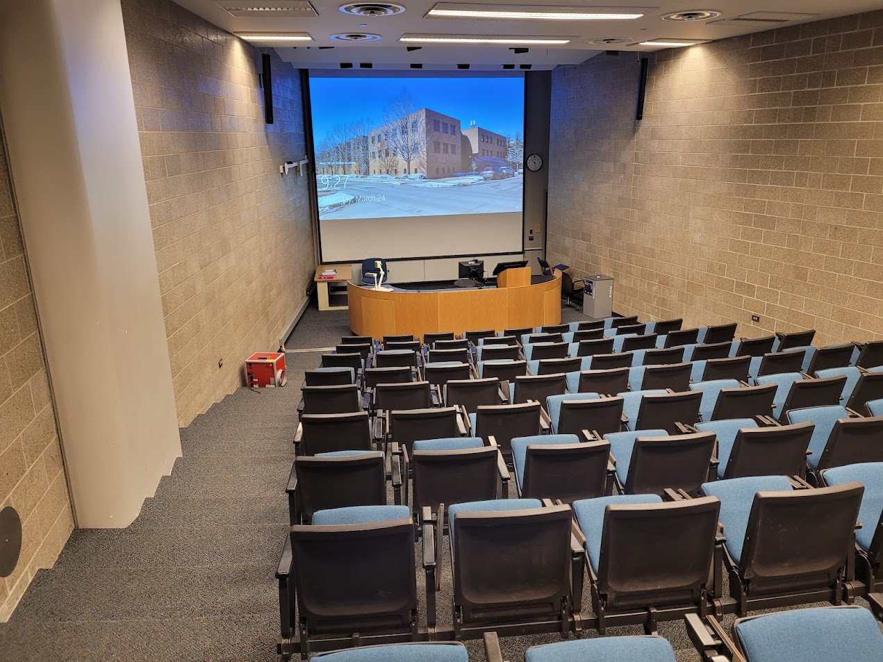 A view of the classroom with theater auditorium seating, white boards, and large lectern in front.
