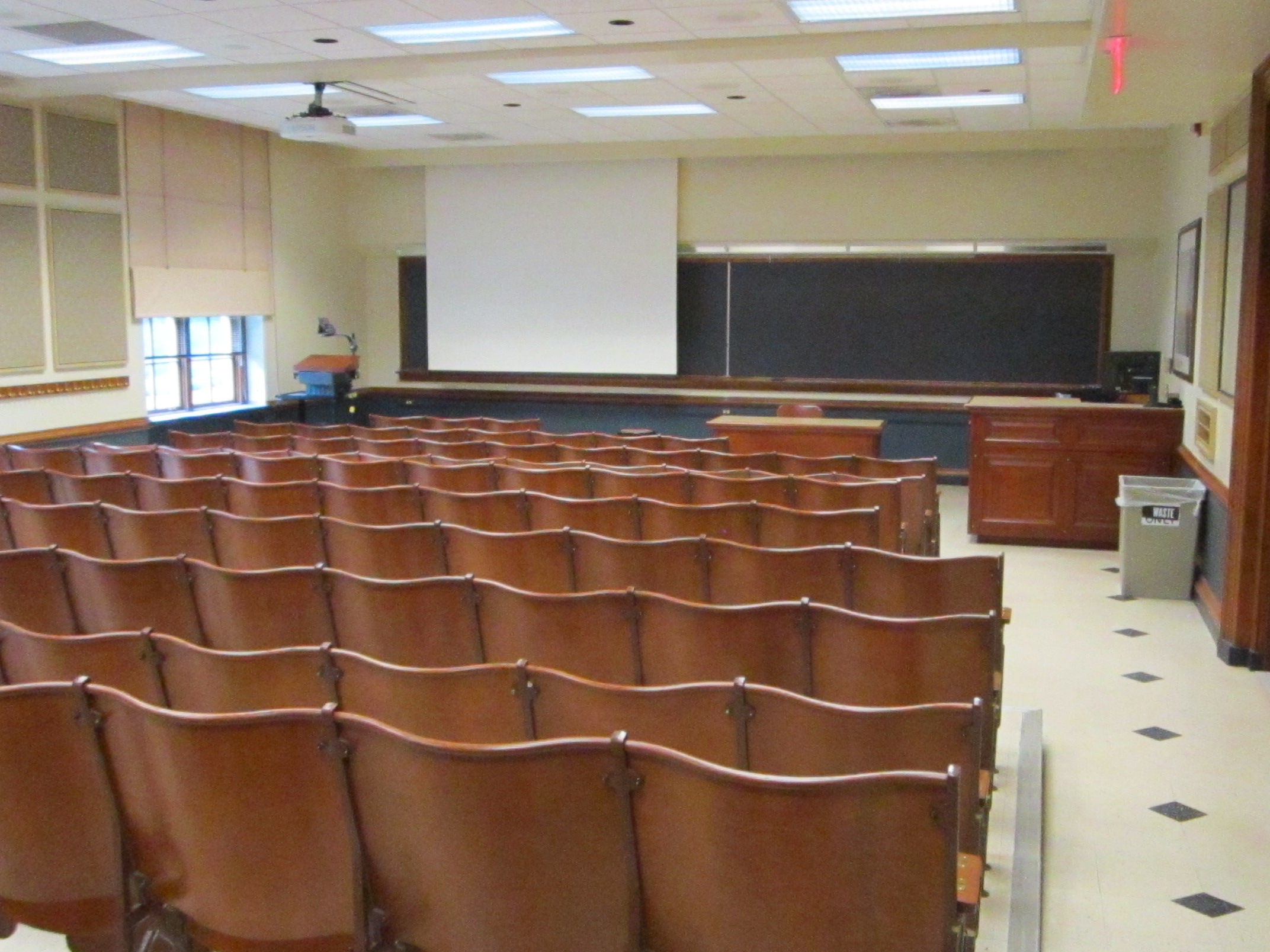 A view of the classroom with theater auditorium seating, chalkboards, and instructor table in front.