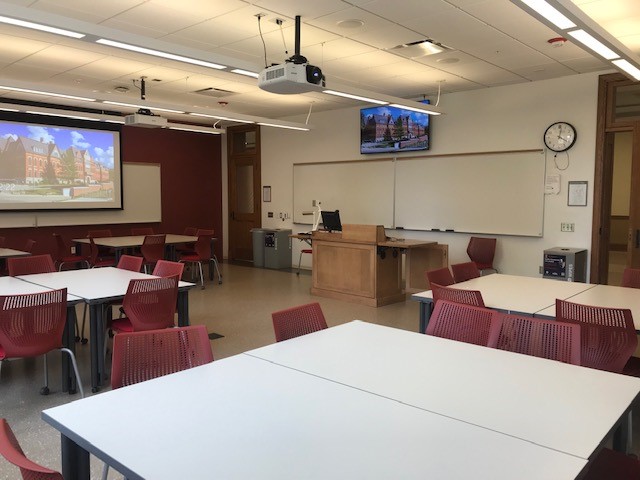 This is a view of the room with student desks, a front lecture table, projection screen, LCD display, and a whiteboard.