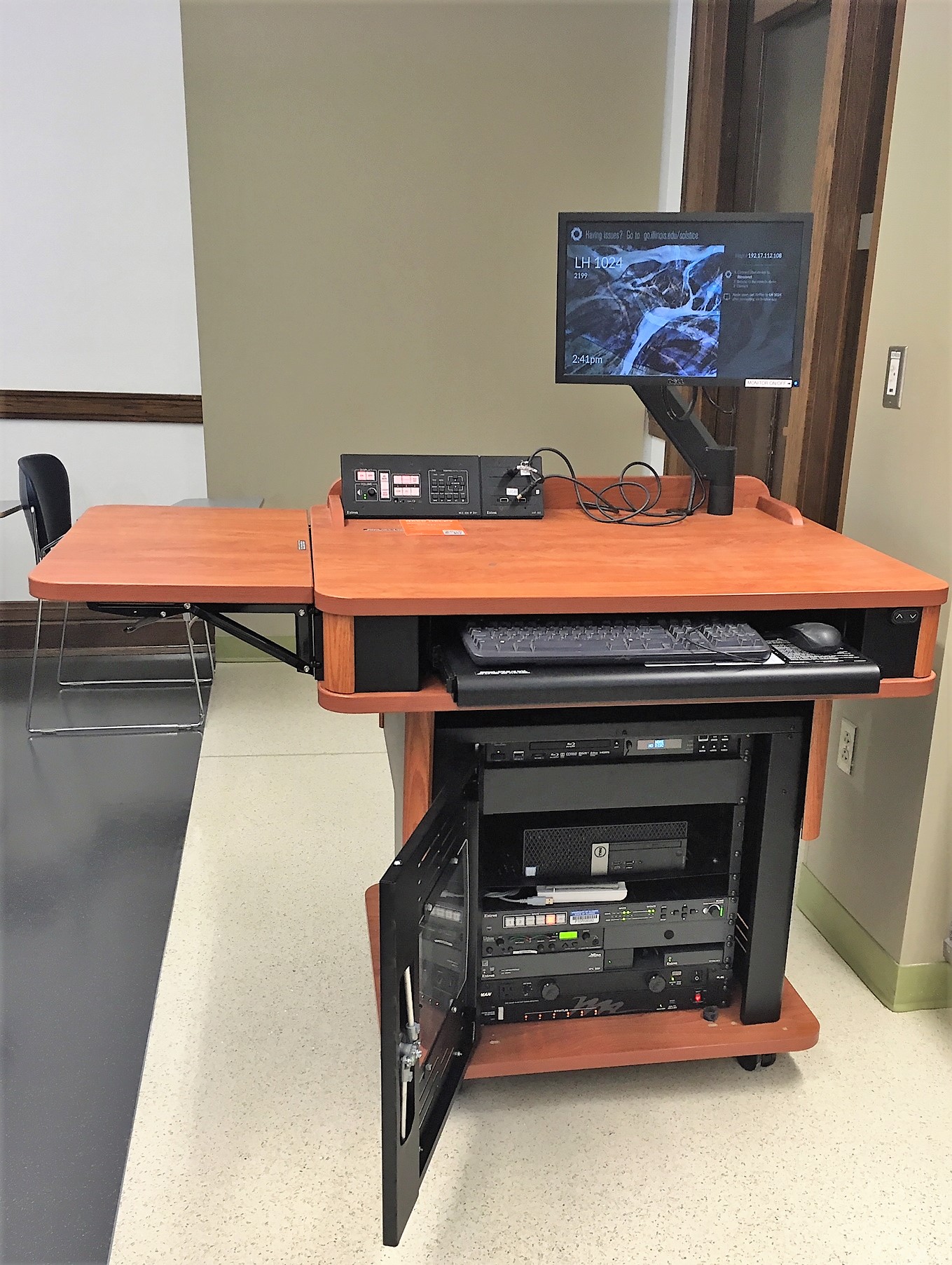 A view of the open cabinet with a computer monitor, HDMI input, a push button controller, and a audio visual rack.