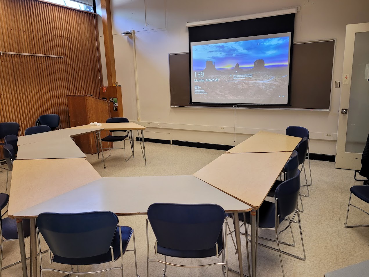 A view of the moveable tables and chairs, chalkboard, and instructor table in front.