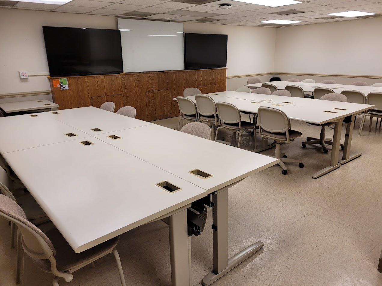 A view of the classroom with student desks, dual flat panel monitors and whiteboard in front.