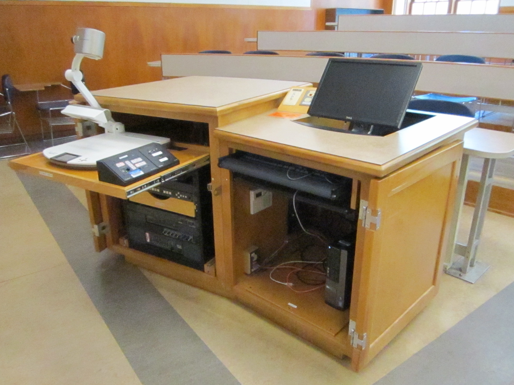 A view of the open cabinet with a computer monitor, HDMI inputs, a push button controller, document camera, audio visual rack and electric screen controls.