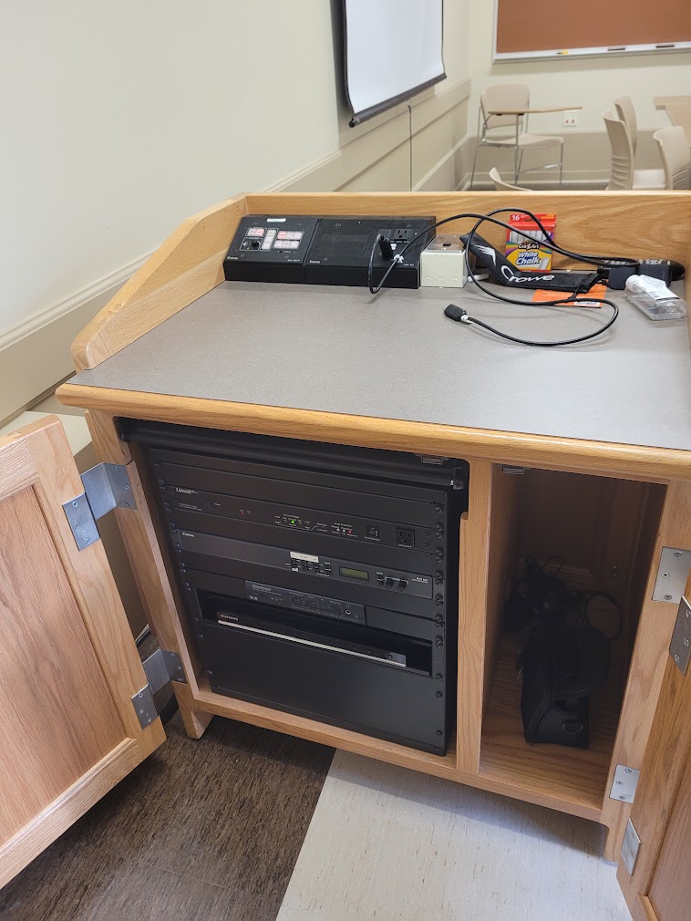 A view of the open cabinet with HDMI inputs, a push button controller and audio visual rack.