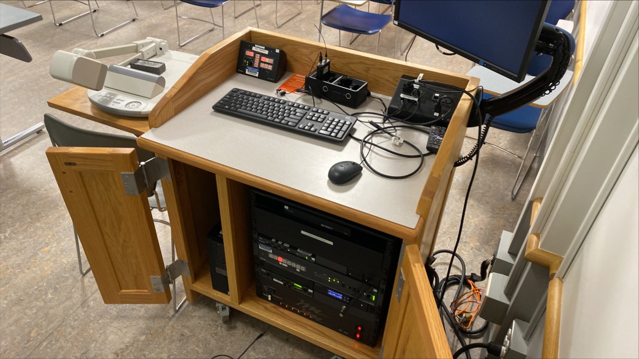 A view of the open cabinet with a computer monitor, VGA and HDMI input, a push button controller, document camera, and audio visual rack.