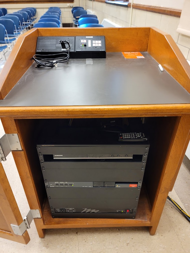 A view of the open cabinet with HDMI inputs, a push button controller, and audio visual rack.