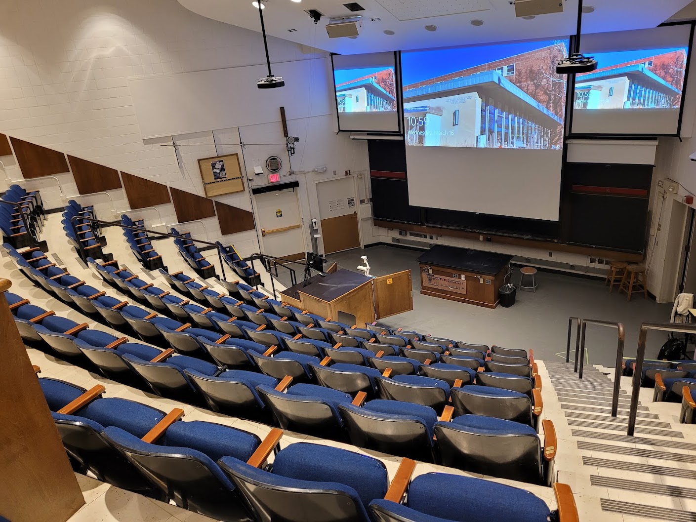 A view of the classroom with Theater Auditorium seating, chalk boards, projection screens, and instructor table in front.