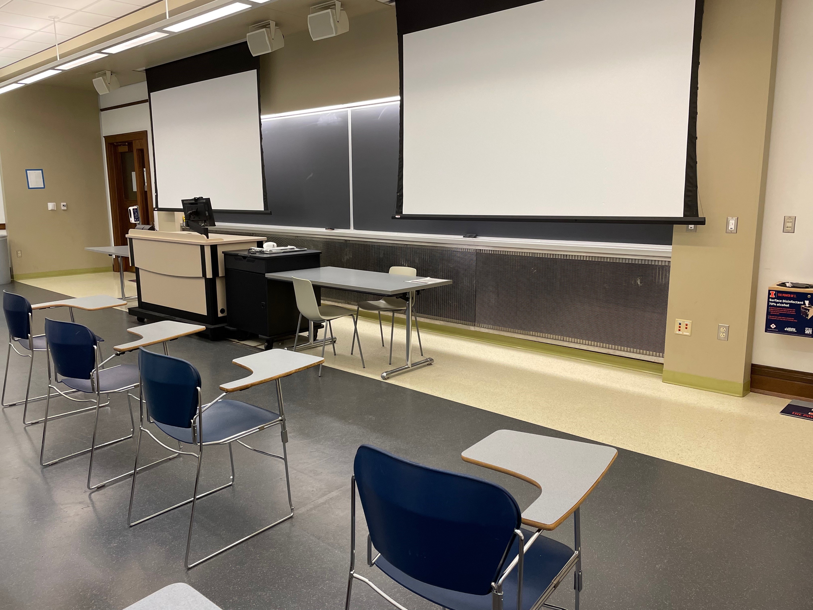 A view of the classroom with moveable tableted arm chairs, chalkboard, and instructor table in front.